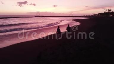 空中飞行。 一男一女在粉红色美丽<strong>的夕阳下</strong>沿着黑色<strong>的</strong>火山海滩<strong>奔跑</strong>.. 特内里费，西班牙。